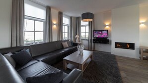 Una sala moderna con sofá, mesa de centro, televisión, chimenea y ventanas grandes.