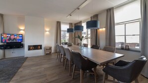 A modern dining area with a long wooden table, several chairs, pendant lights, a flat-screen TV, and a fireplace. - Holiday Home in Colijnsplaat by the Sea (Colijnsplaat)