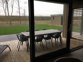Un patio con mesa y sillas, una terraza de madera y vistas a una zona ajardinada y un edificio.