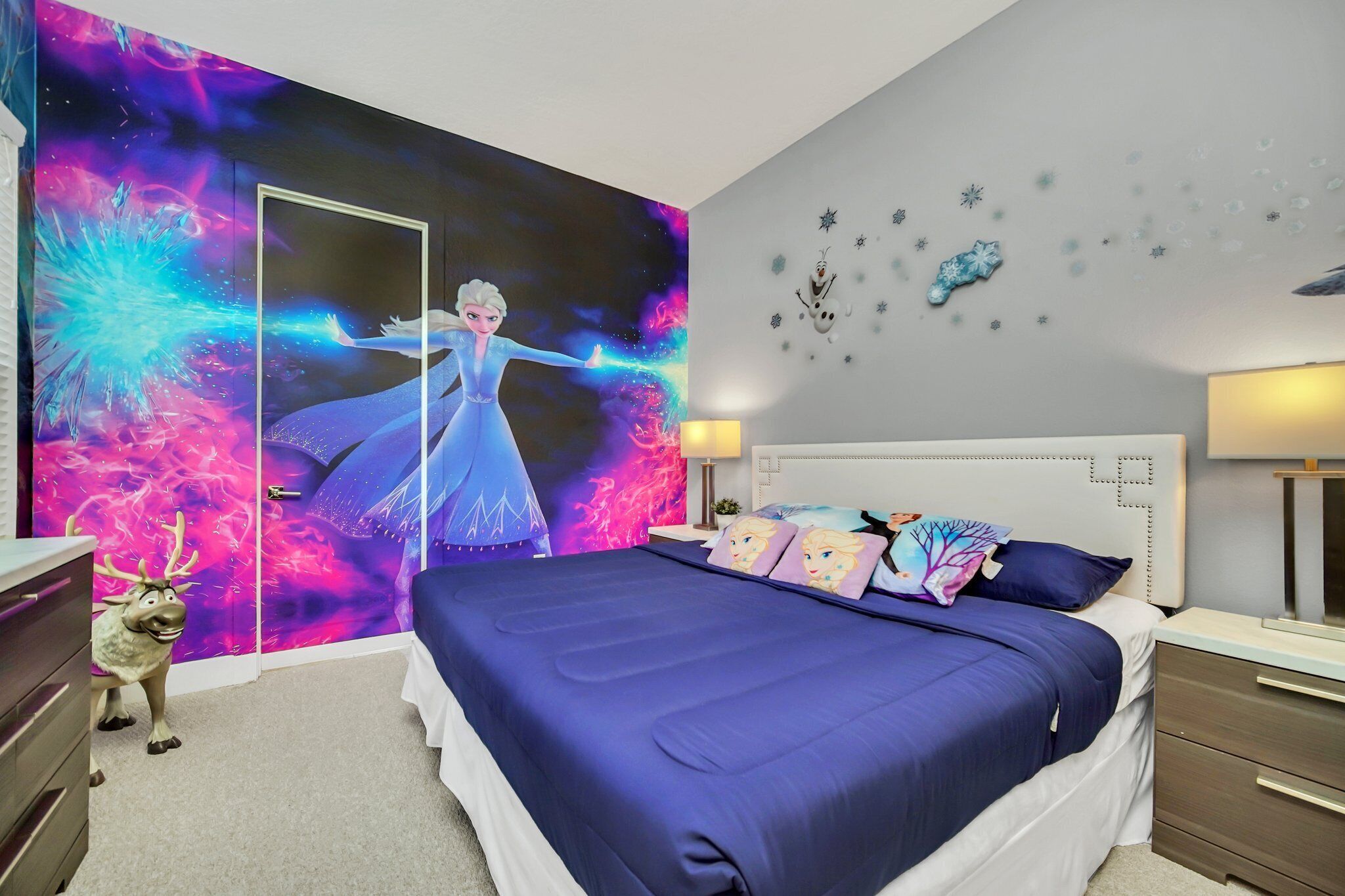 Een slaapkamer met een groot bed, een dressoir, een spiegel en een muur met een ruimtethema wanddecoratie.