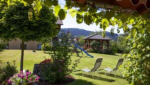 A garden with a playground, two lounge chairs, and a pergola. - Relaxing Apartment With Sauna (Ruhmannsfelden)