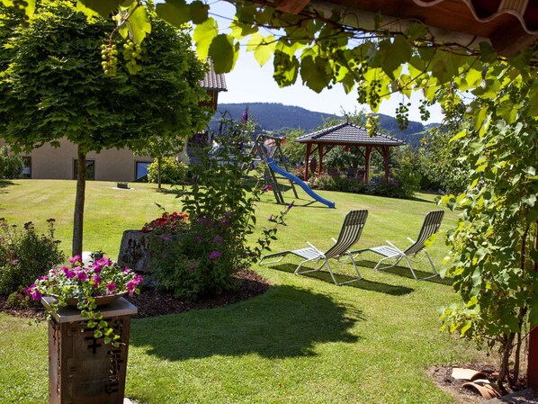 A garden with a playground, two lounge chairs, and a pergola.