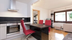 A modern kitchen with a black countertop, stainless steel appliances, and red chairs. There is a dining table with a black table runner and a white sofa in the adjacent living area. - Relaxing Apartment With Sauna (Ruhmannsfelden)