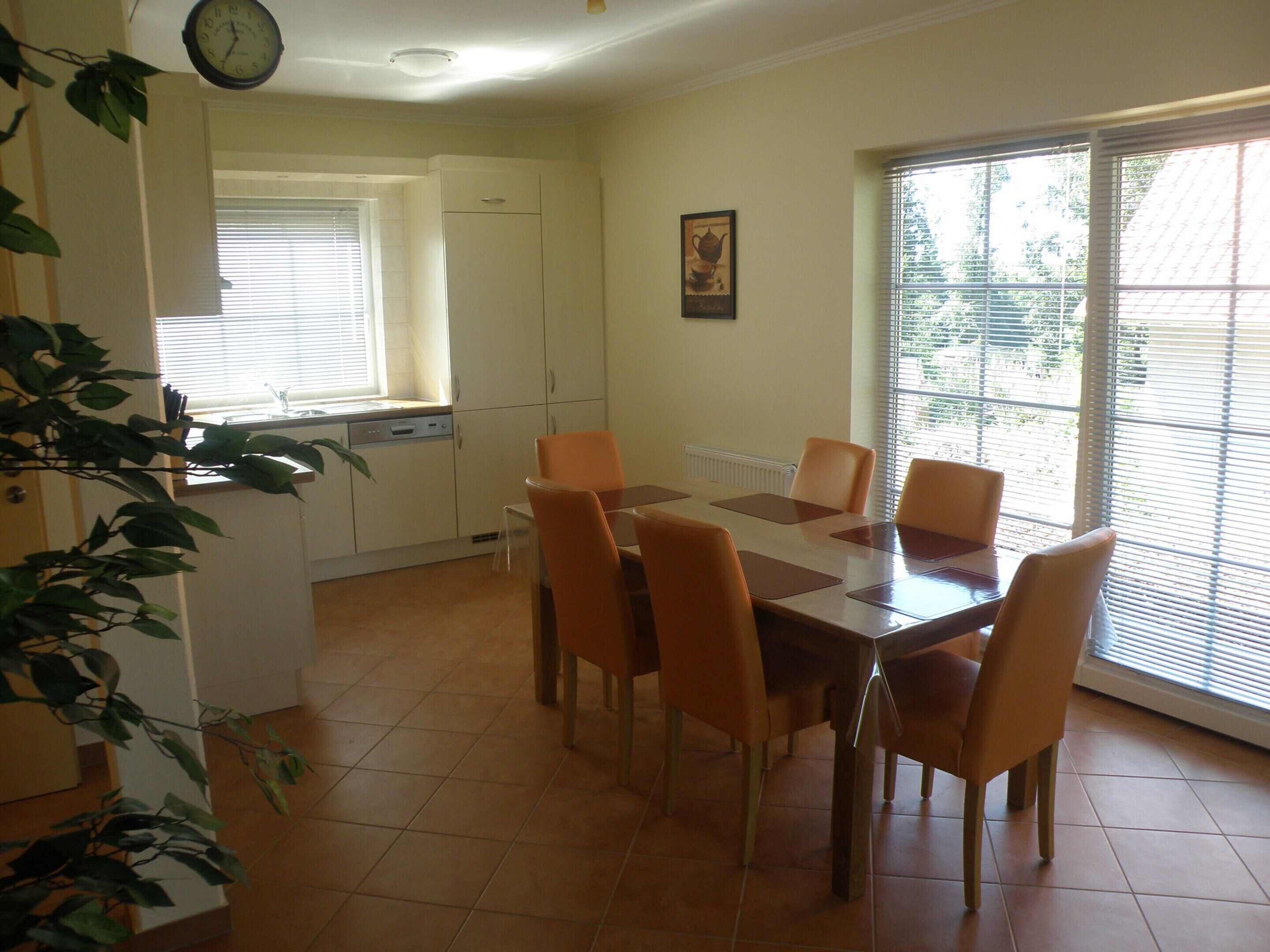 A dining area with a table and chairs, a clock on the wall, and a window with blinds.