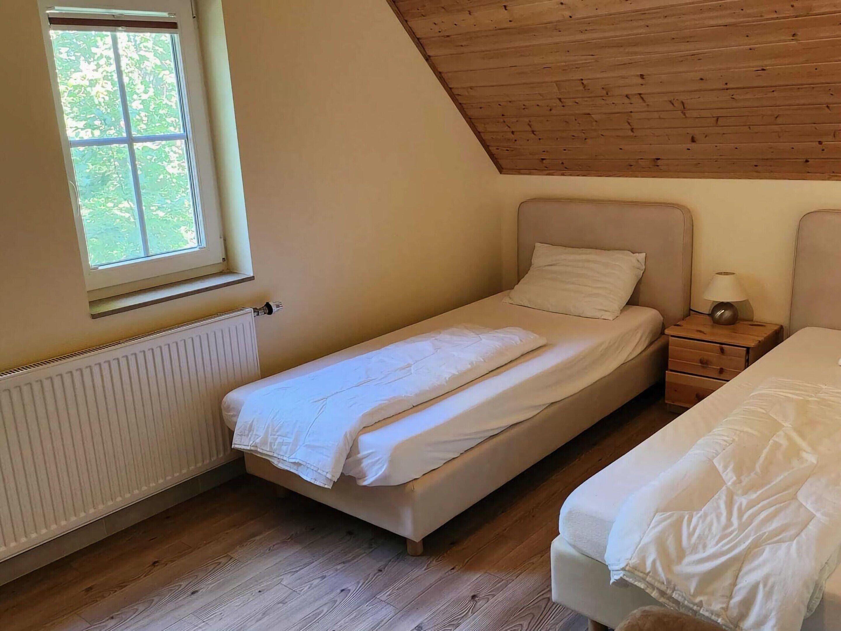 Un dormitorio pequeño de una sola habitación con techo inclinado, una ventana, un radiador y dos camas.