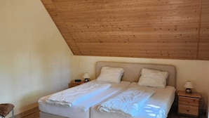 A double bed with two nightstands, a wooden ceiling, and a small chair. - Tidy House With Sauna and Steam Bath, in a Forest (Brandscheid)