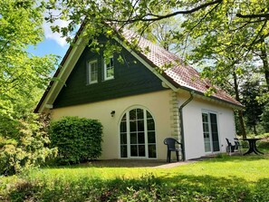 A two-story house with a green roof and beige walls, surrounded by lush greenery. - Tidy House With Sauna and Steam Bath, in a Forest (Brandscheid)