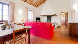 A spacious living area with a wooden ceiling, a red sofa, a dining table with chairs, and a fireplace. - Rustic Farmhouse in Terricciola (Terricciola)