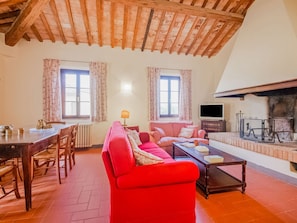 A cozy living room with a wooden ceiling, a red sofa, a dining table with chairs, and a fireplace. - Rustic Farmhouse in Terricciola (Terricciola)