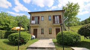 A stone building with a balcony, steps leading to the entrance, and a garden with a lamp post and umbrella. - Apartment in Marche With Pool and Privacy (Apecchio)