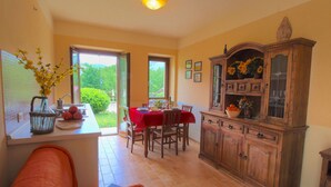 A dining area with a red tablecloth, a wooden cabinet with glass doors, and a view through a glass door to an outdoor garden. - Apartment in Marche With Pool and Privacy (Apecchio)