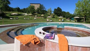 A swimming pool with a hot tub, lounge chairs, and umbrellas, surrounded by greenery and a distant building. - Apartment in Marche With Pool and Privacy (Apecchio)