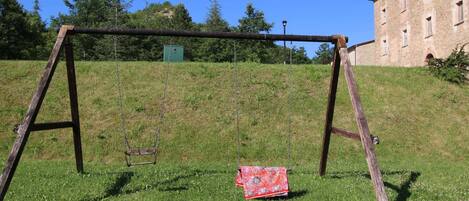 A swing set in a grassy area with a building in the background.