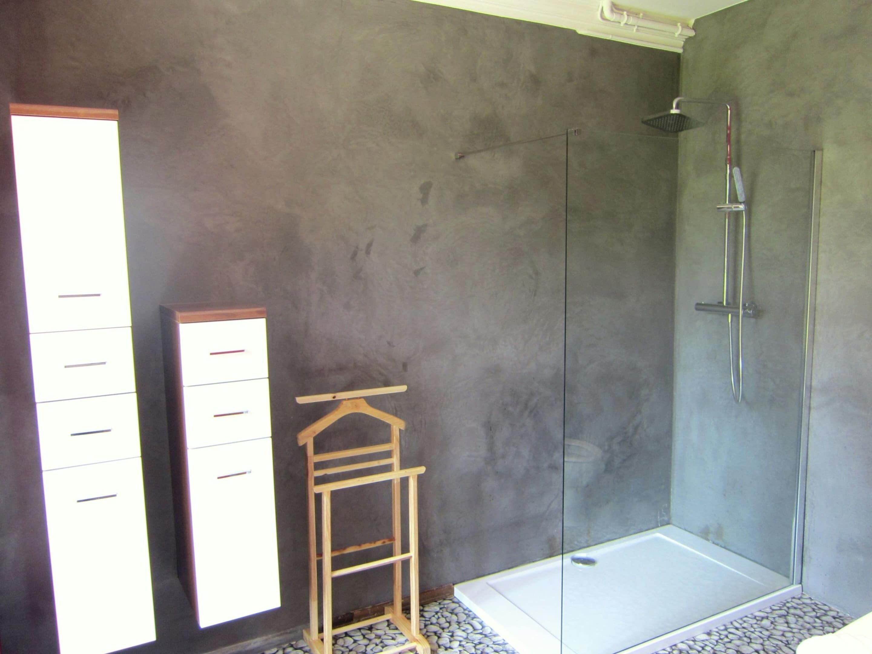 A bathroom with a walk-in shower, a wooden hanger rack, and a tiled floor.