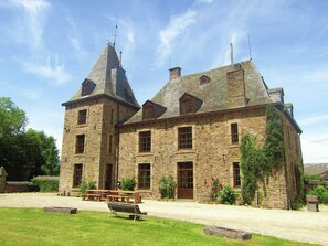 A stone building with a central tower and two smaller towers, surrounded by a well-maintained lawn and a picnic table. - Luxury Castle, Basse-bodeux (Trois-Ponts)