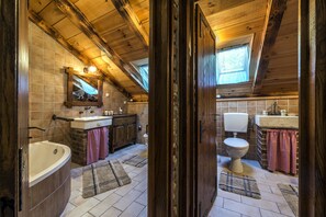 Ein rustikales Badezimmer mit Holzbalkendecke, einer Badewanne, einer Toilette und einem Waschbecken.