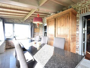 A dining area with a granite table, wooden cabinets, and a hanging light fixture. - Appealing Chalet in Westouter With Garden (Heuvelland)
