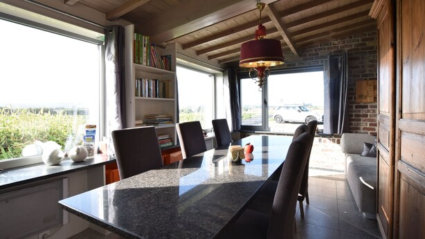 Zona pranzo con tavolo in granito, sedie, una libreria e vista sulla campagna.