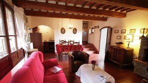 A cozy living room with a red sofa, a dining table with chairs, a fireplace, and a staircase leading upstairs. - Quaint Cottage With Pool (Anghiari)