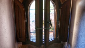 Una puerta con dos contraventanas de madera, un pomo de metal y vistas a un muro de piedra y follaje.