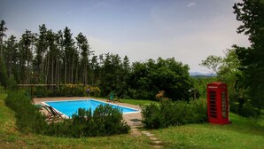 Une piscine entourée de verdure, une cabine téléphonique rouge et un ciel dégagé.