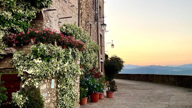 Un bâtiment en pierre doté d’une cour, de plantes en pot et offrant une vue sur des montagnes lointaines.