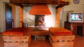 A fireplace with a brick surround, two red cushioned benches, and a television on a wooden cabinet. - Belvilla by OYO La Verbena (Montalcino)