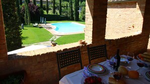 A patio with a table set for dining, overlooking a swimming pool and lush garden. - Belvilla by OYO La Verbena (Montalcino)