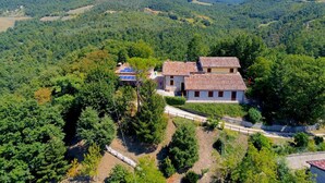 Una casa rural con tejado de baldosas, rodeada de un bosque denso y colinas.