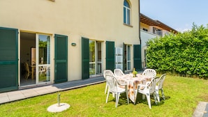Een huis met twee verdiepingen met een patio, voorzien van een ronde tafel en witte stoelen.