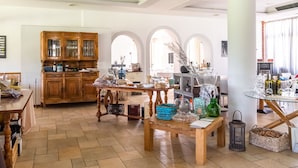 Een ruime keuken met houten kastjes, een eettafel met diverse spullen, en uitzicht op de woonkamer met rondboogvensters.