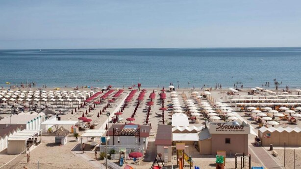 Een strandhotel met rijen ligbedden en parasols, een zwembad en een helder uitzicht op zee.
