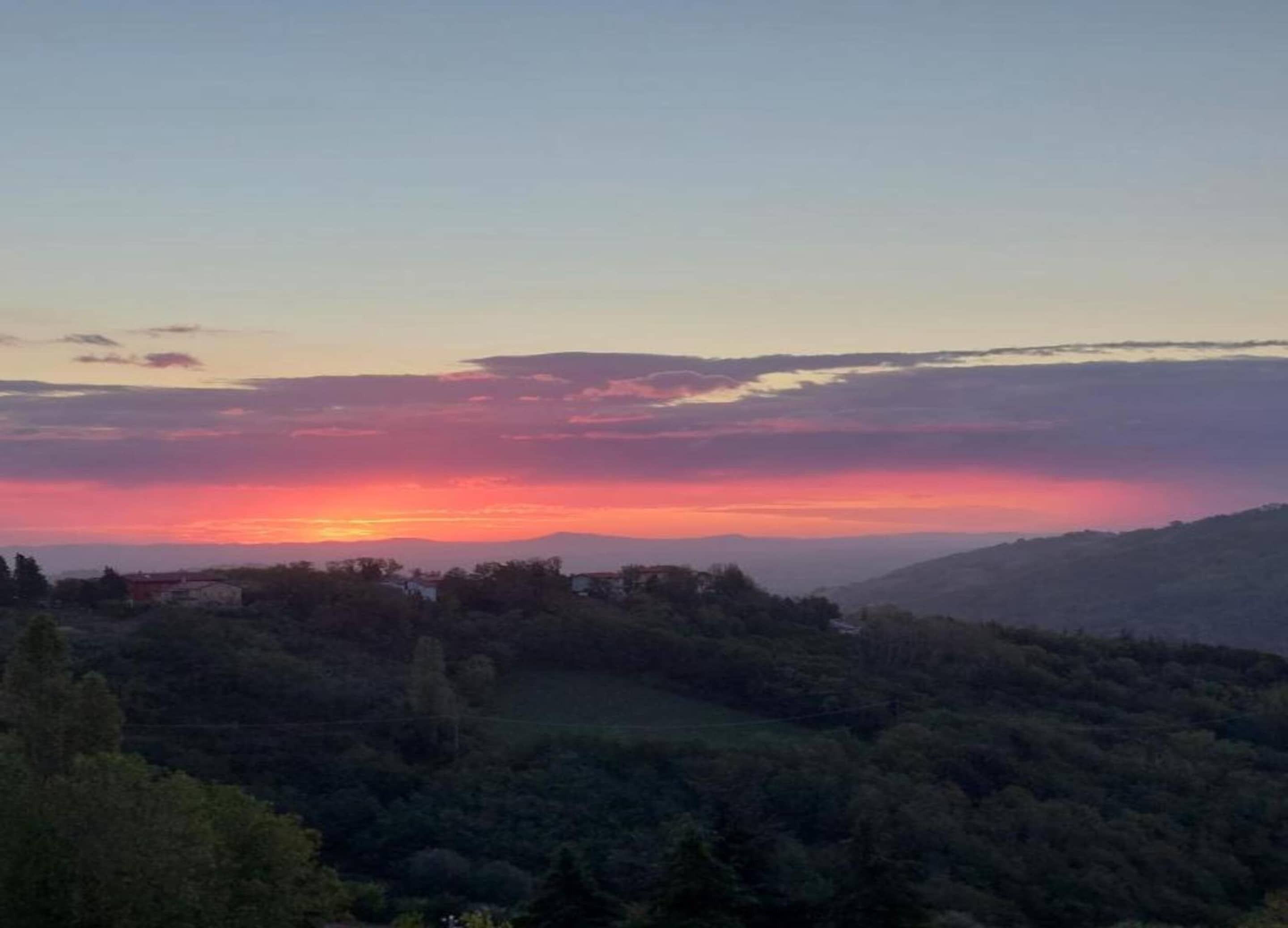 A sunset over a hilly landscape with scattered trees and buildings.