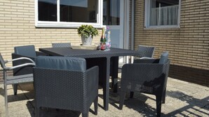 En udendørs patio med et bord, stole, en potteplante og en champagneflaske.