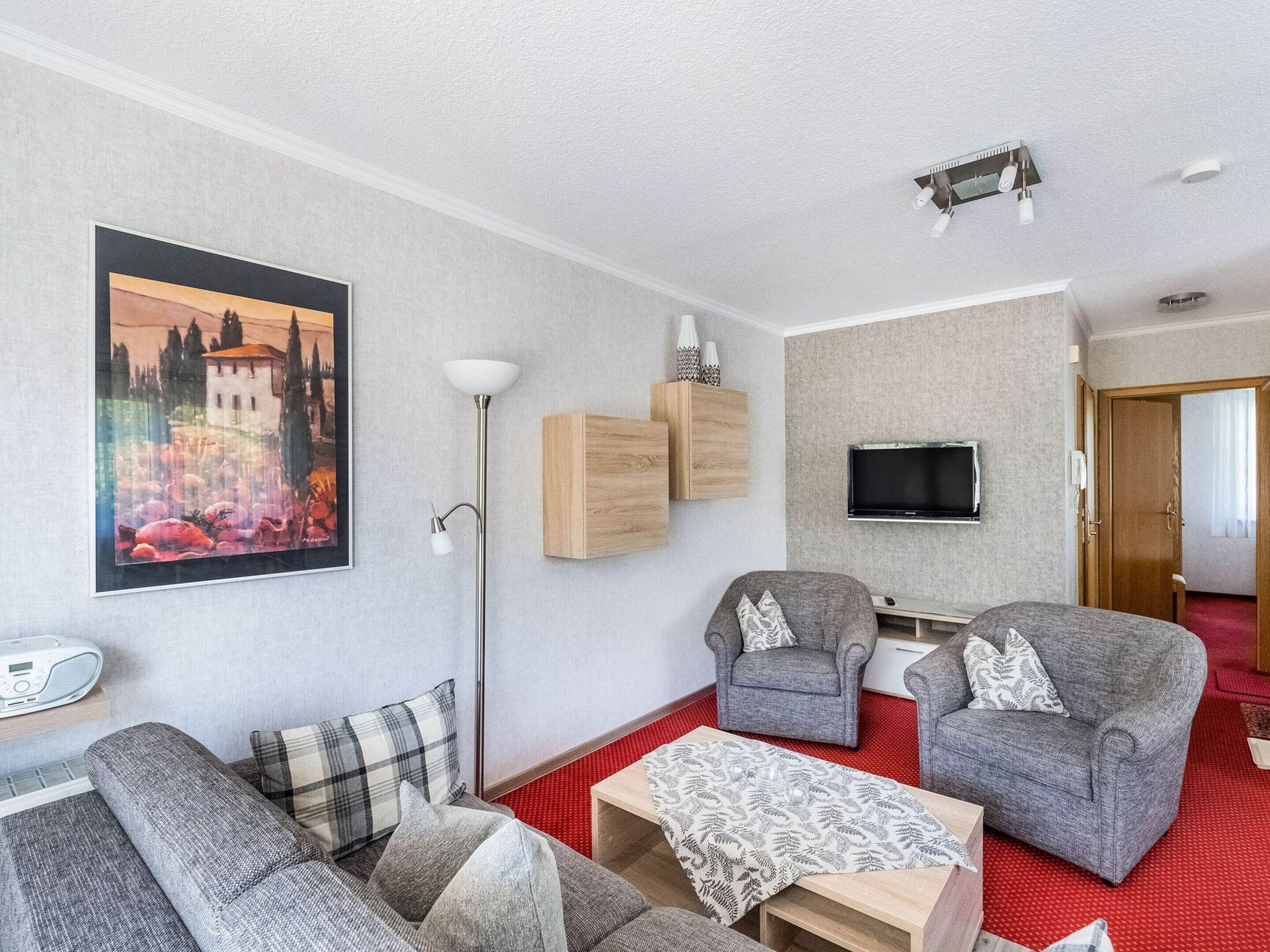 A modern living room with a sofa, two armchairs, a coffee table, a floor lamp, a TV, and a painting on the wall.