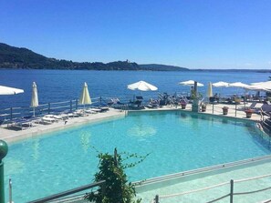A poolside area with lounge chairs and umbrellas, overlooking a body of water and hills. - Brand new and Elegant Residence on Lake Maggiore (Meina)