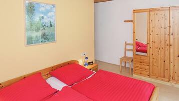 A bedroom with two beds, a wooden wardrobe, a chair, and a painting on the wall.