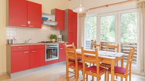 Uma cozinha moderna com armários vermelhos, uma mesa de jantar de madeira com cadeiras e uma janela grande com vista para o verde.