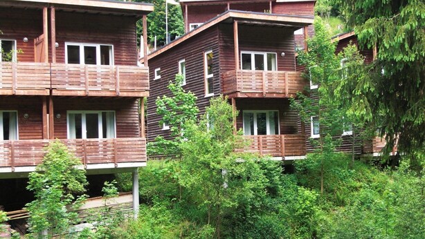 Fileira de cabanas de madeira com varandas, rodeadas por vegetação densa.
