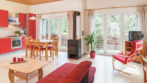 Uma sala moderna com sofá, mesa de jantar e cadeiras, cozinha com armários vermelhos, lareira e janelas amplas com cortinas.