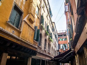 A narrow street with old buildings, some with balconies and shutters.