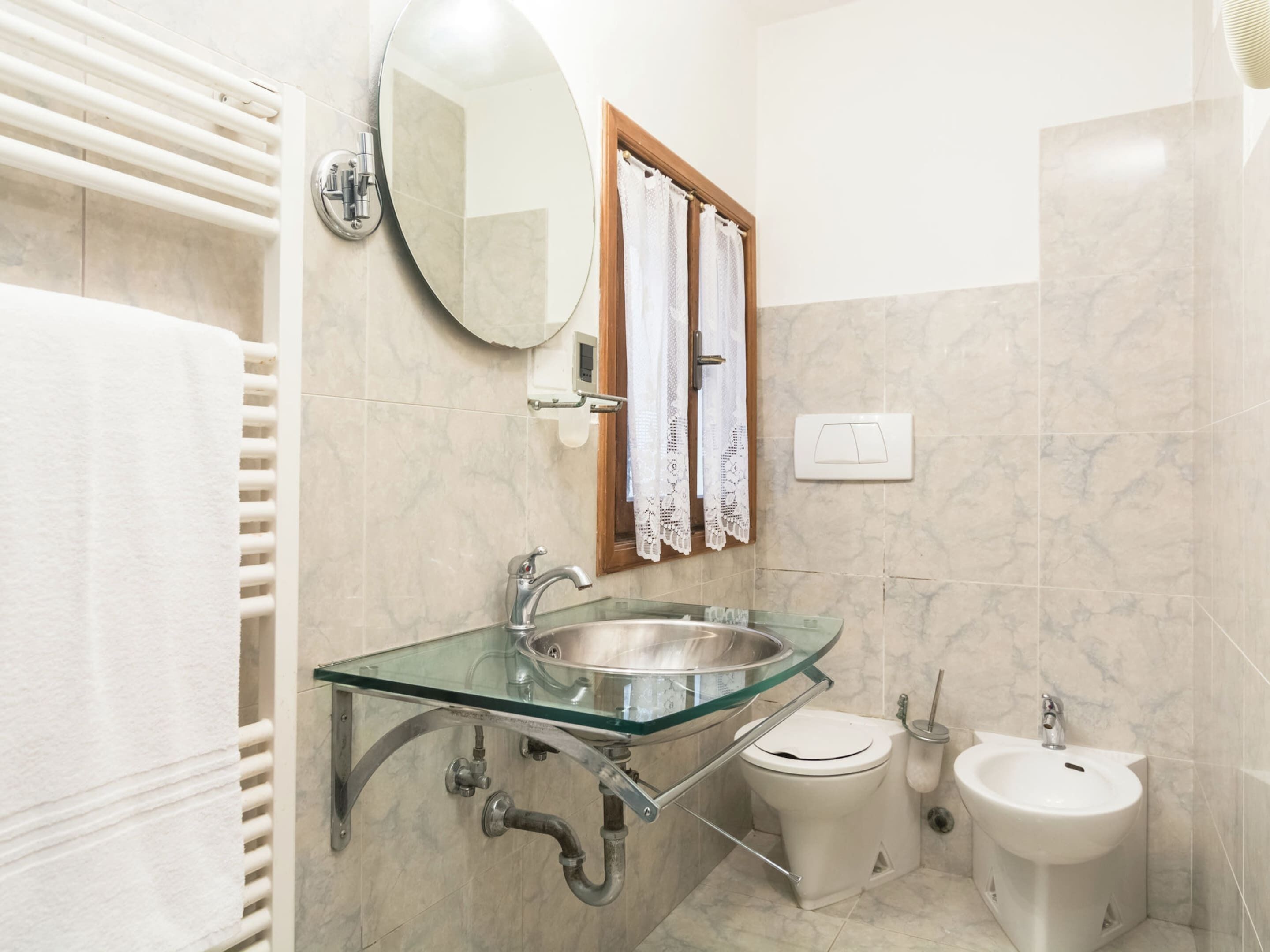 Un baño con lavabo de vidrio, inodoro, bidé, toallero y espejo.