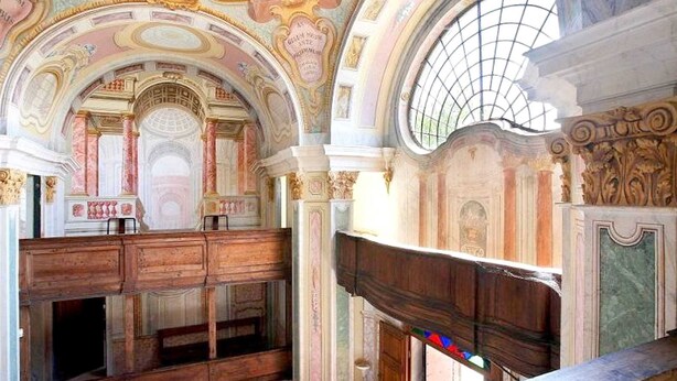 An ornate interior with a wooden bench, a high ceiling with intricate designs, and a large arched window. - Belvilla by OYO Apartment in Castle With Garden (Rocca Grimalda)