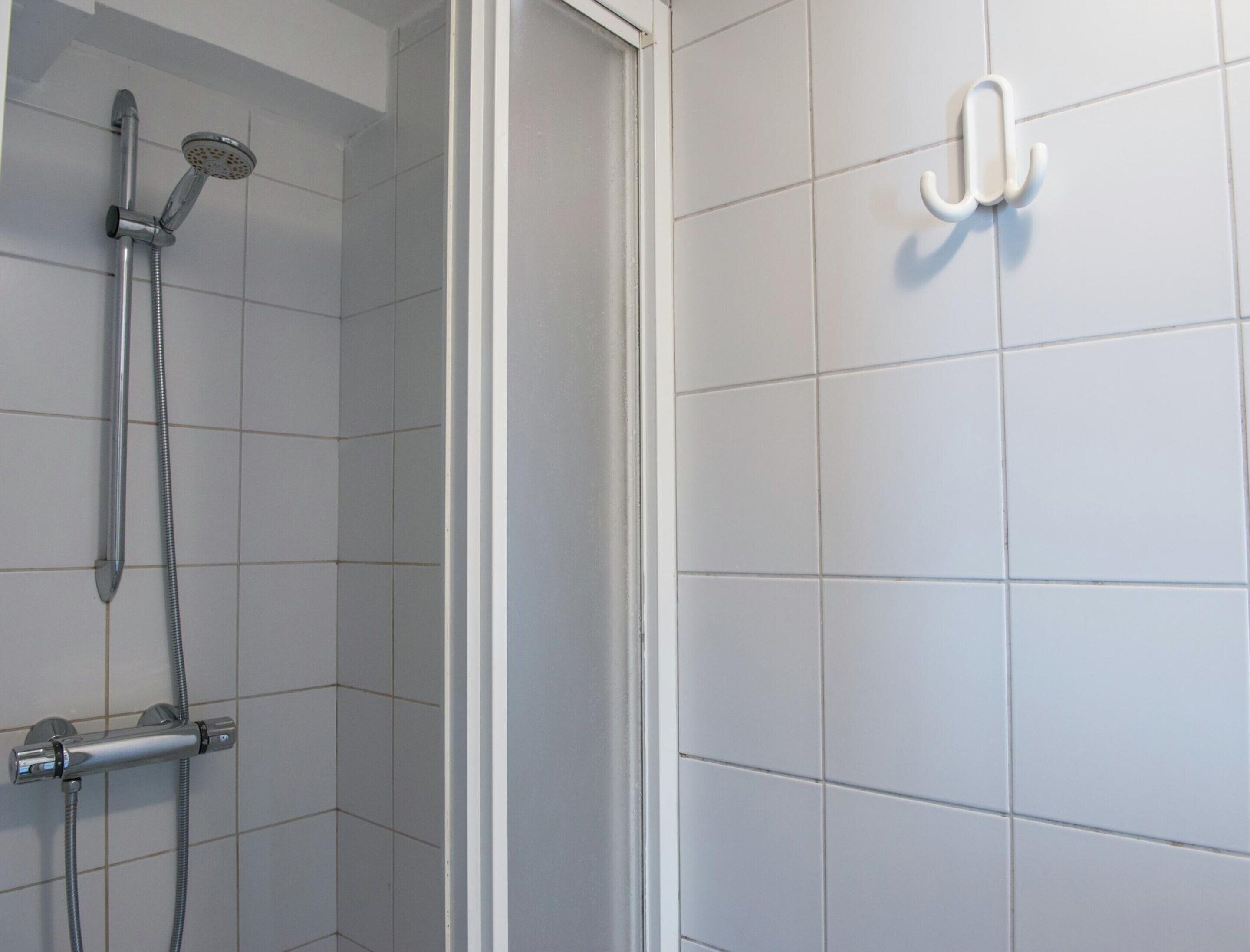 Ein Badezimmer mit weißen Fliesen, einer Dusche inklusive Handbrause und Wandarmatur sowie einem Handtuchhalter.