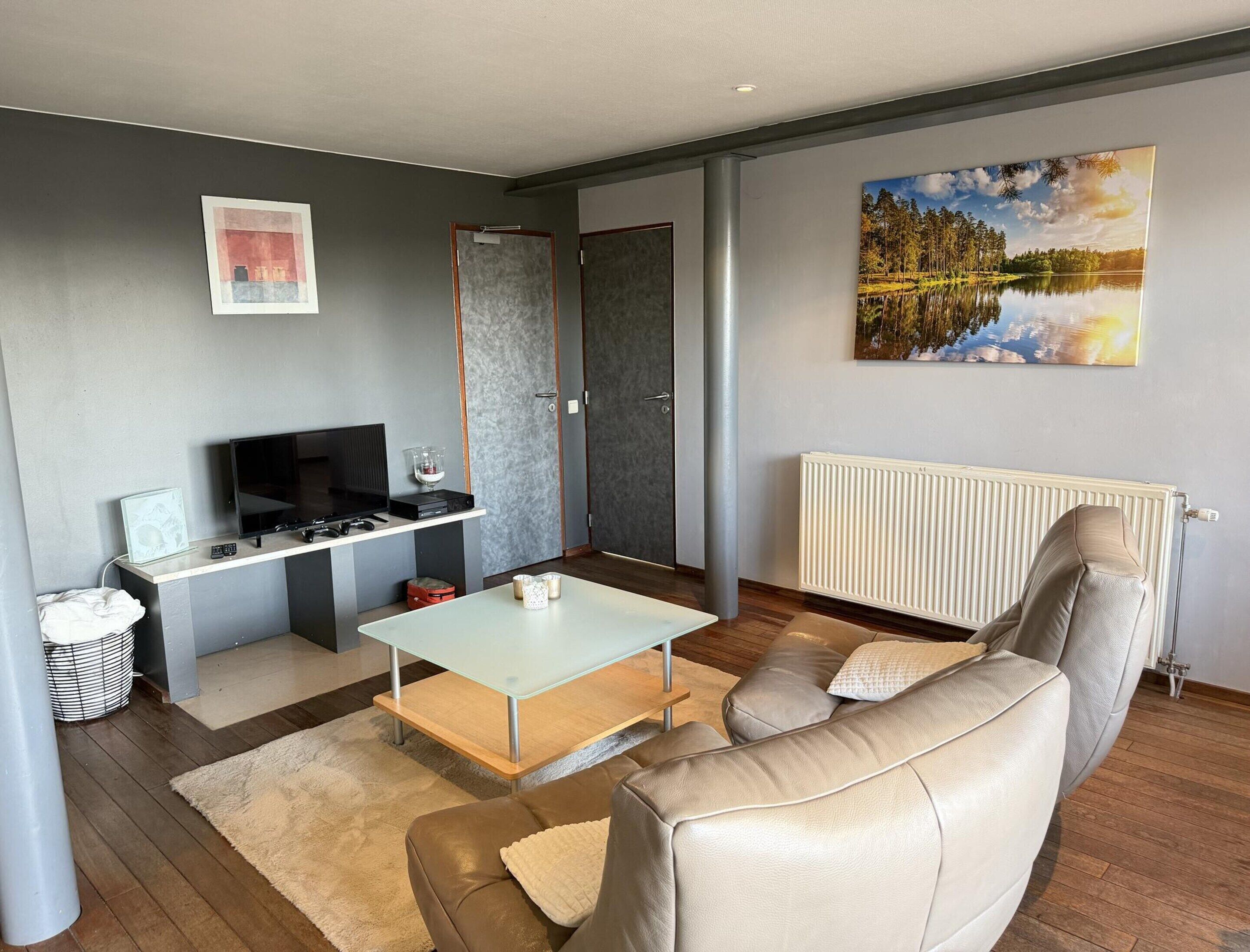 A modern living room with a sofa, a coffee table, a TV, and a painting on the wall.