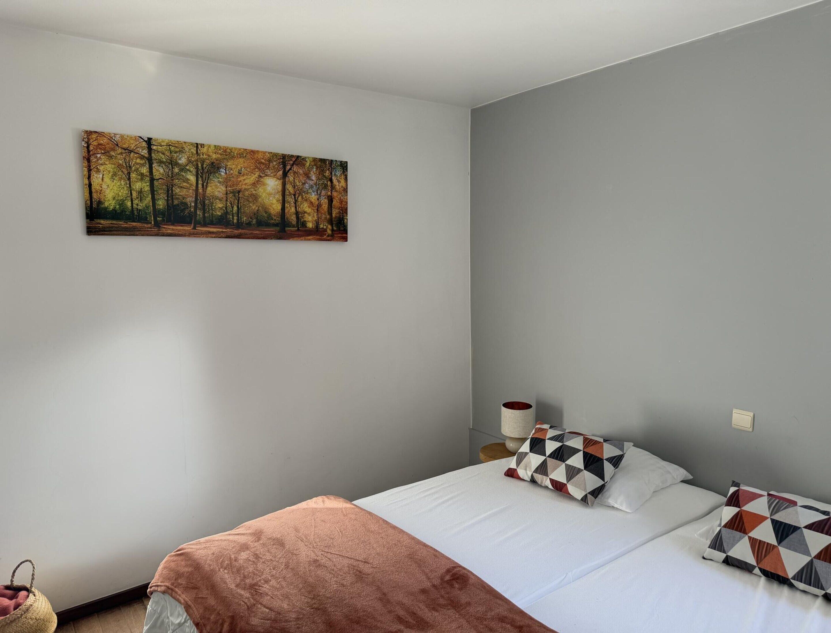 Une chambre à coucher avec un lit, des oreillers, une table de chevet, une lampe et un tableau au mur.