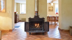 A room with a wood-burning stove, tiled floor, wooden furniture, and a painting on the wall. - Castle Wing Situated in the Heart of a Quiet (Manhay)