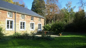 A two-story brick building with a sloped roof, multiple windows, and a small garden area with a bench. - Castle Wing Situated in the Heart of a Quiet (Manhay)