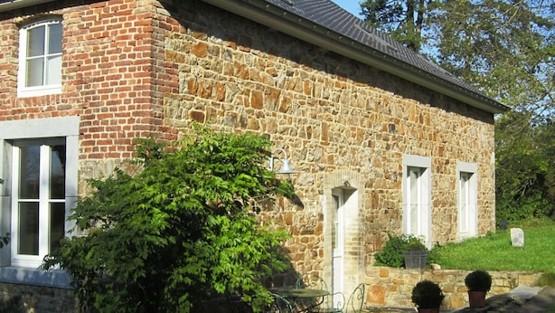 A stone building with a brick facade, white windows, and a small garden area with potted plants. - Castle Wing Situated in the Heart of a Quiet (Manhay)
