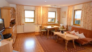 A cozy living room with a wooden dining table, a sofa, and a TV. - Bavaria Modern Family Stay (Prackenbach)